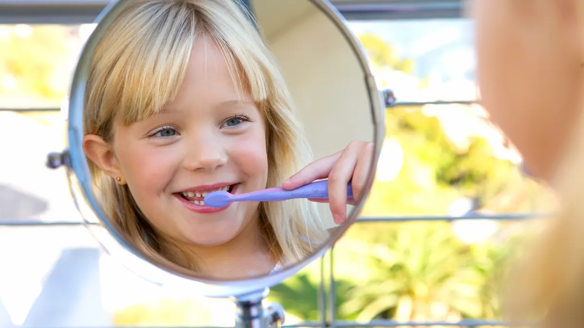 smiling girl brushing her teeth, reflected in a round mirror